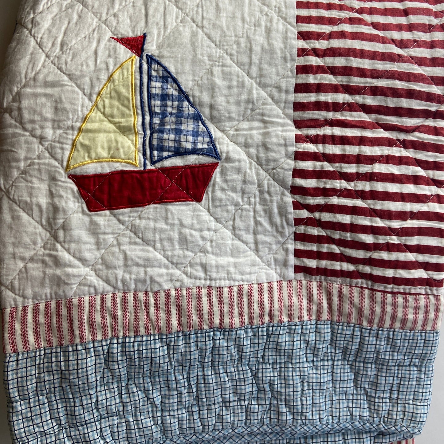Quilt with patchwork design featuring a sailboat emblem on a plain background