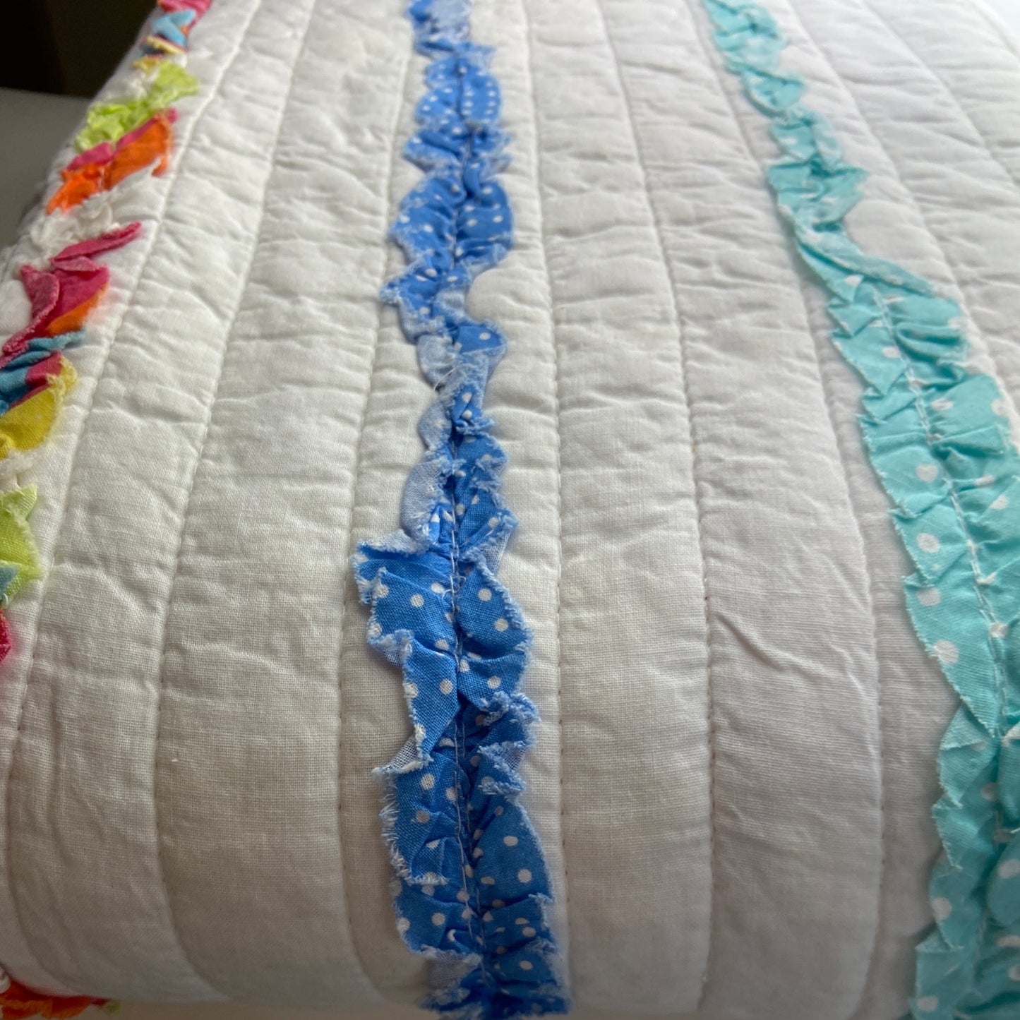 Quilt with blue ruffled trim on a white background
