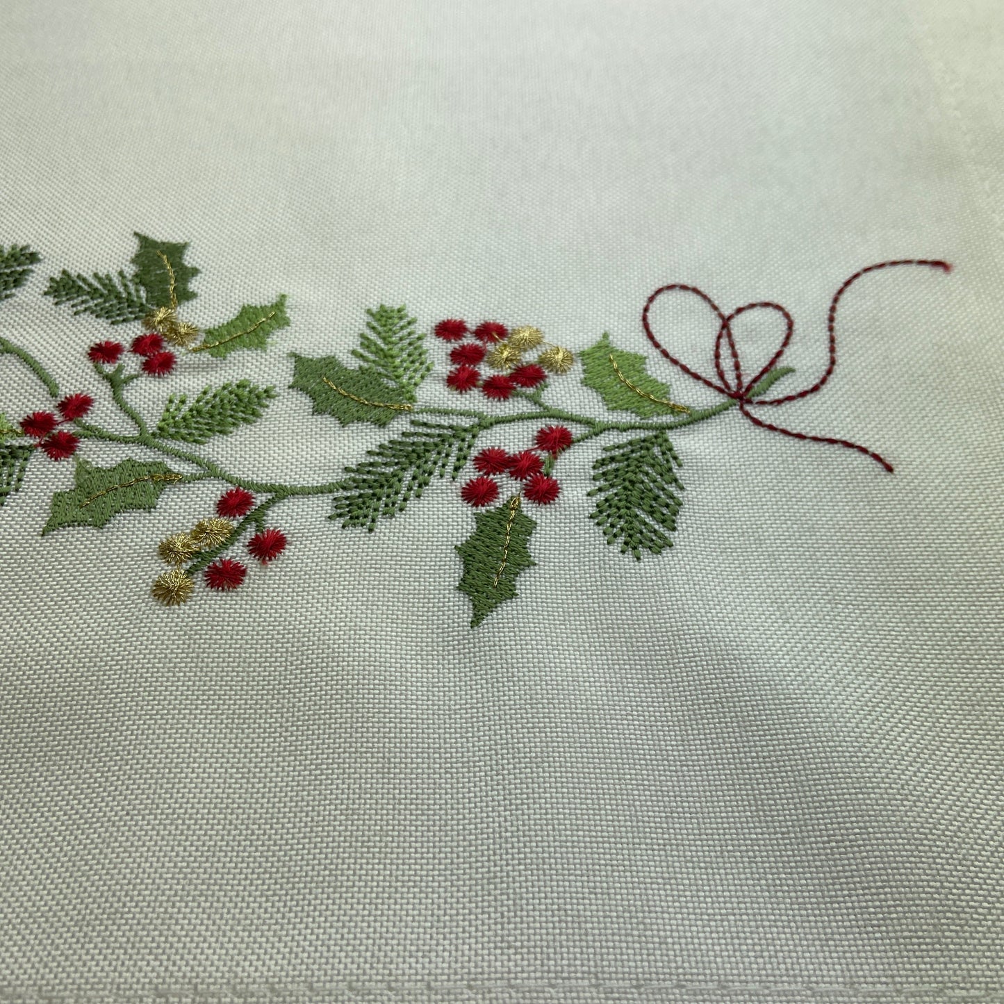 Embroidered holly berry design on a white fabric background