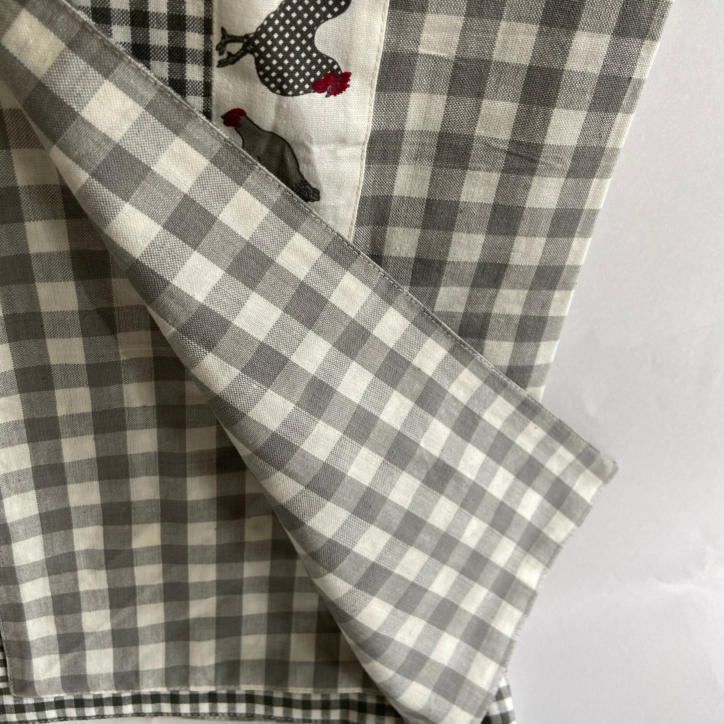 Gray and white checkered fabric with embroidered chickens on a white background