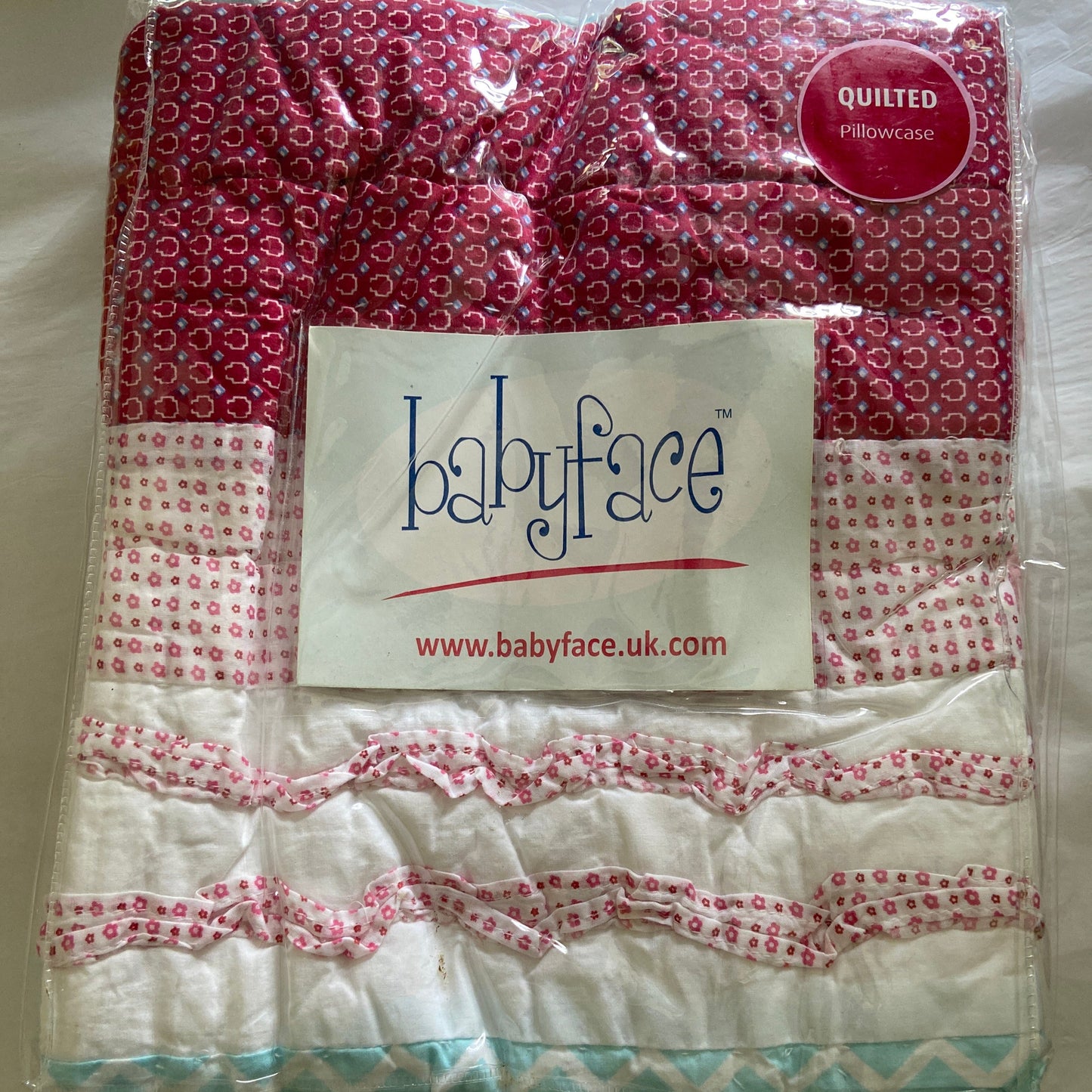 Quilt with pink and white pattern on a plain background, featuring a visible brand label.