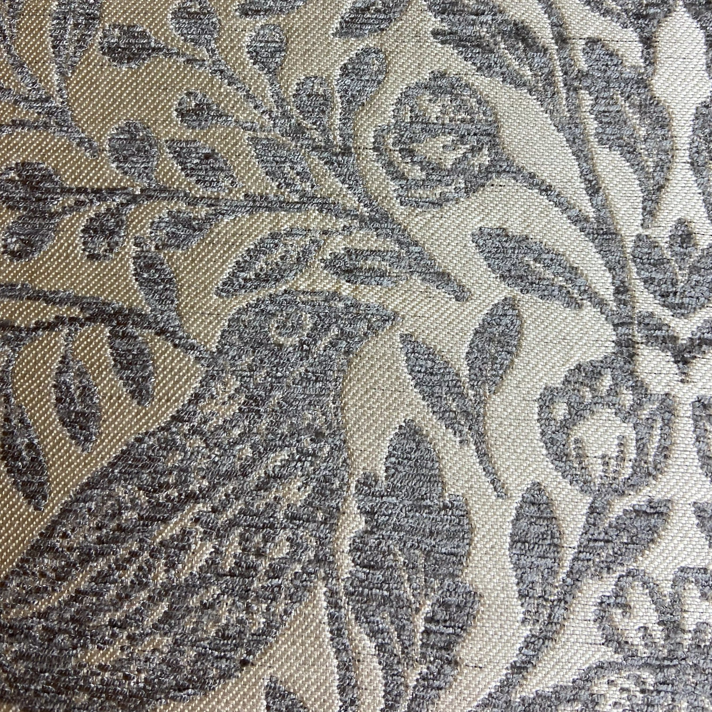 Close-up of a textured fabric with a leaf pattern in gray and beige.