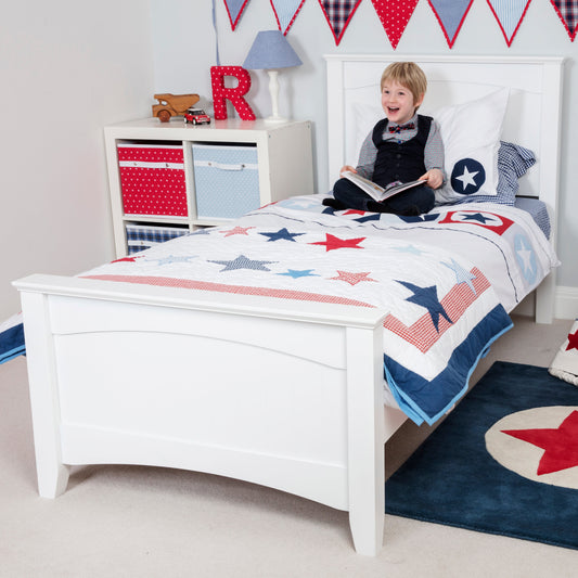 Child in a bedroom with a white bed, star-themed bedding, and red and blue accents.