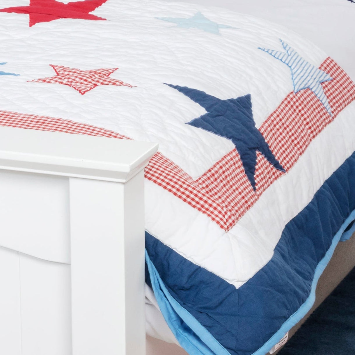 Child in a bedroom with a white bed, star-themed bedding, and red and blue accents.