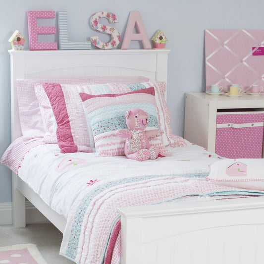 Children's bedroom with pink and white bedding, decor, and storage boxes.