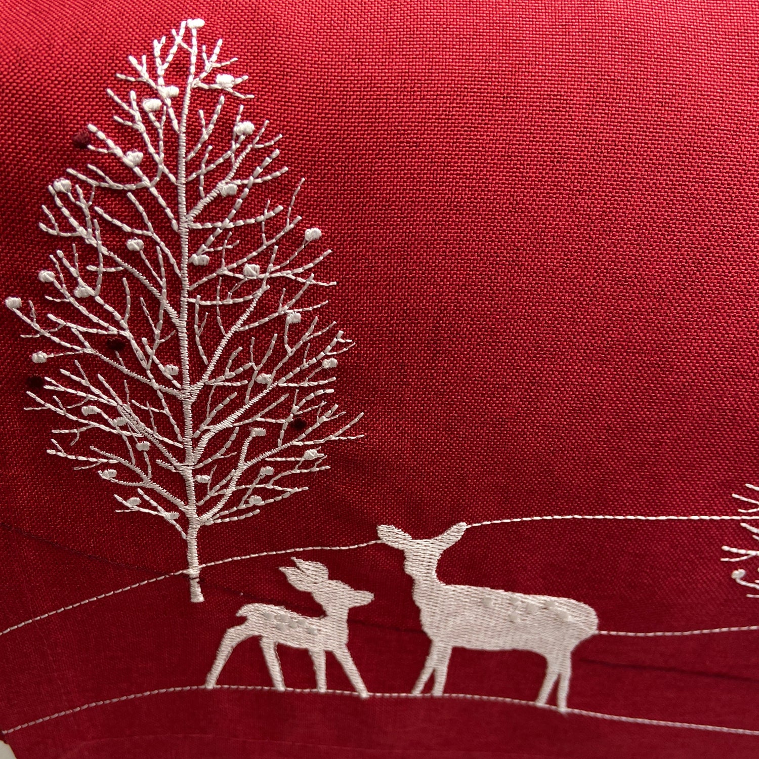 Red fabric with white embroidered designs of a leaf and deer on a plain background