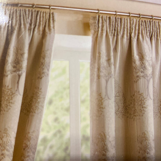 Arden Pencil Pleat Curtains by Belfield Furnishings. These fully lined pencil pleat curtains are set on a natural background with trees embroidered in silver grey and pale gold. Face and lining 100% polyester.