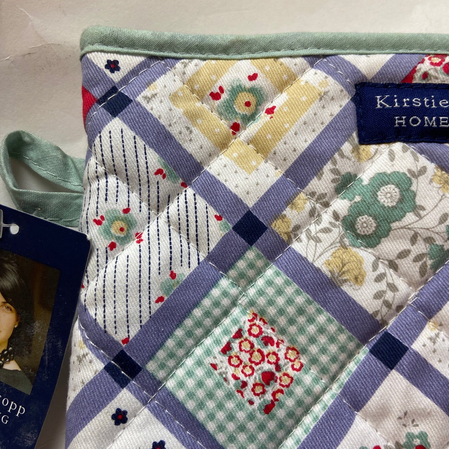Quilt with patchwork design featuring various patterns and colors, branded 'Kirstie Home'.