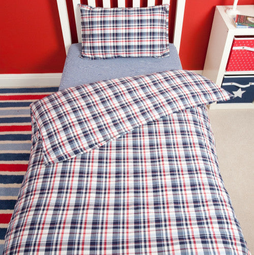Plaid bedding set on a bed with a red wall and striped rug in the background