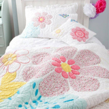 Floral quilt set on a bed with decorative pillows and letters spelling 'BEA'.
